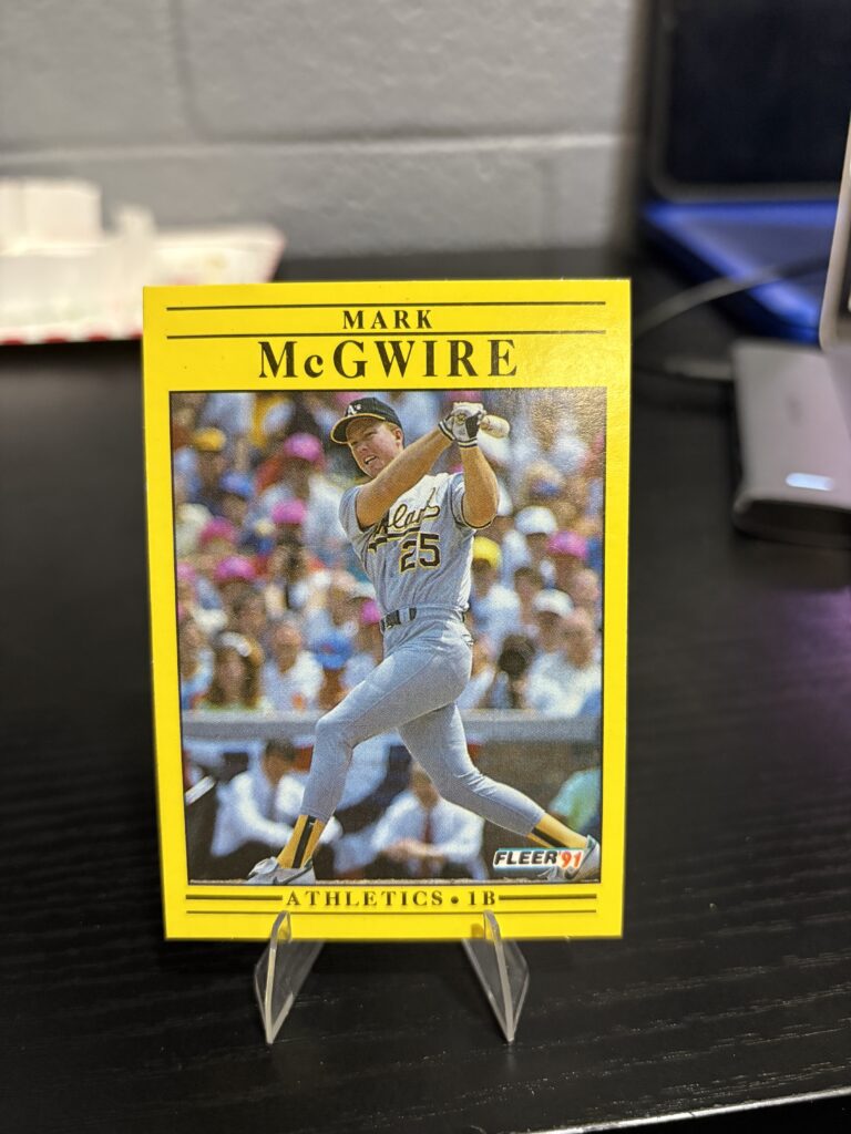 Oakland Athletics Mark McGwire 1991 Fleer baseball trading card, powerful swinging action shot in protective sleeve, high quality vintage rare collectible in clear display case for serious baseball fans and investors today.