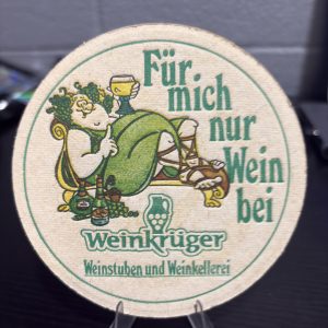 Rare vintage circular "Weinkrüger" winery coaster featuring playful illustrated branding, a high-vibration collectible perfect for enthusiasts of international wine memorabilia looking to manifest prosperity today.