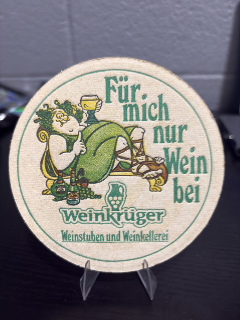 Rare vintage circular "Weinkrüger" winery coaster featuring playful illustrated branding, a high-vibration collectible perfect for enthusiasts of international wine memorabilia looking to manifest prosperity today.