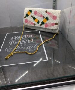 White beaded clutch purse featuring the words Pour More with colorful cocktail designs and a gold chain strap