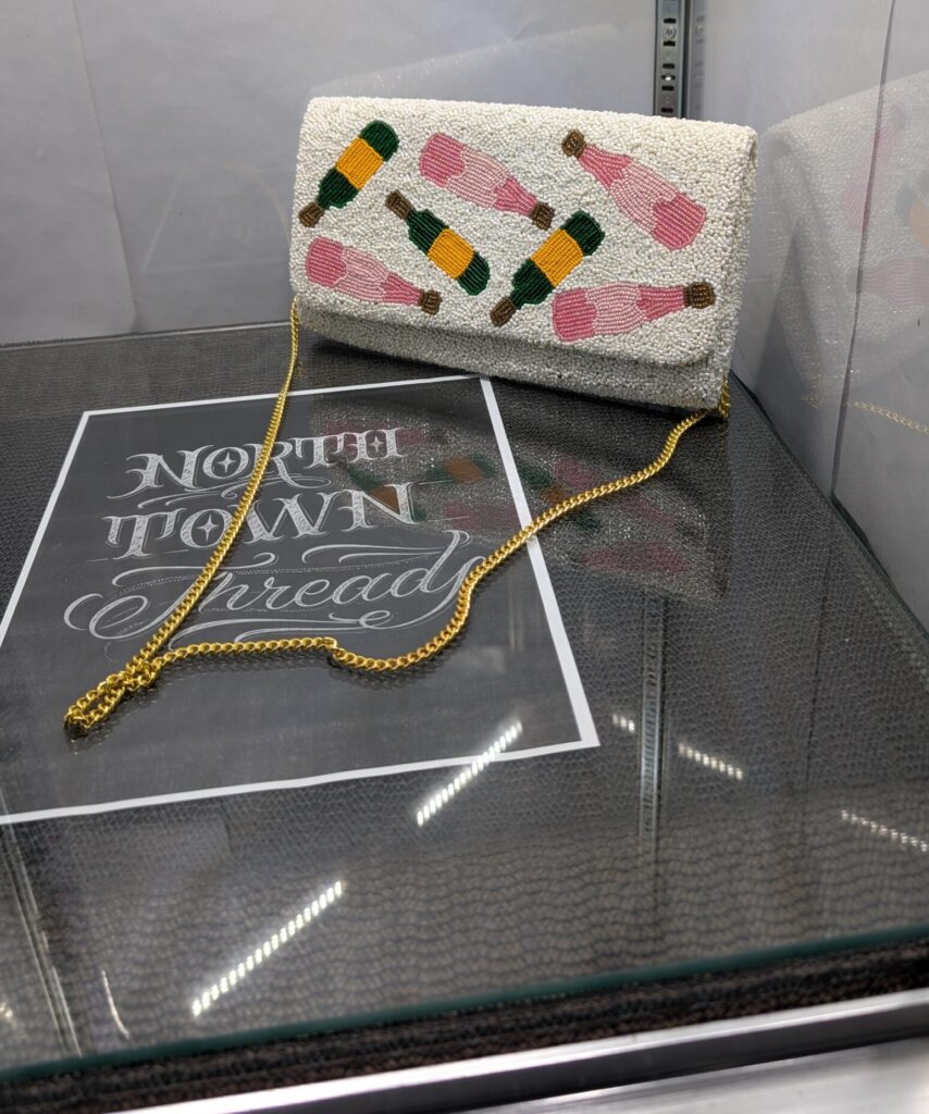 White beaded clutch purse featuring the words Pour More with colorful cocktail designs and a gold chain strap