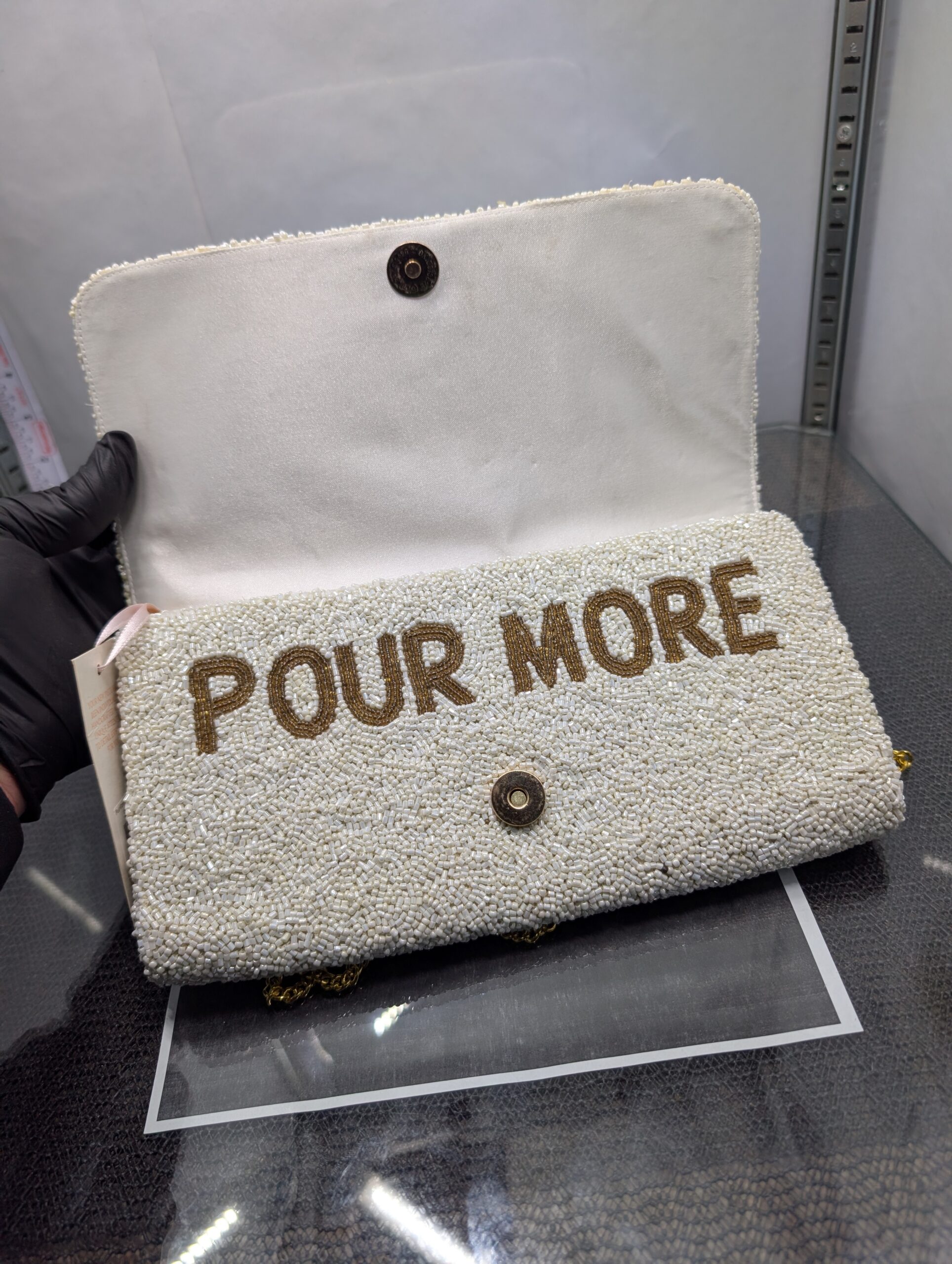 White beaded clutch purse featuring the words Pour More with colorful cocktail designs and a gold chain strap