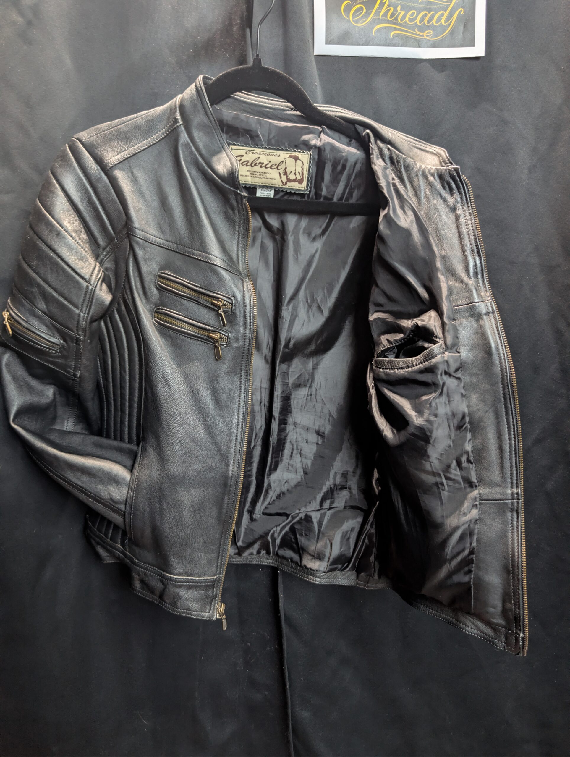 Black genuine sheepskin leather motorcycle jacket by Creaciones Gabriel featuring ribbed shoulder details and brass zipper pockets.