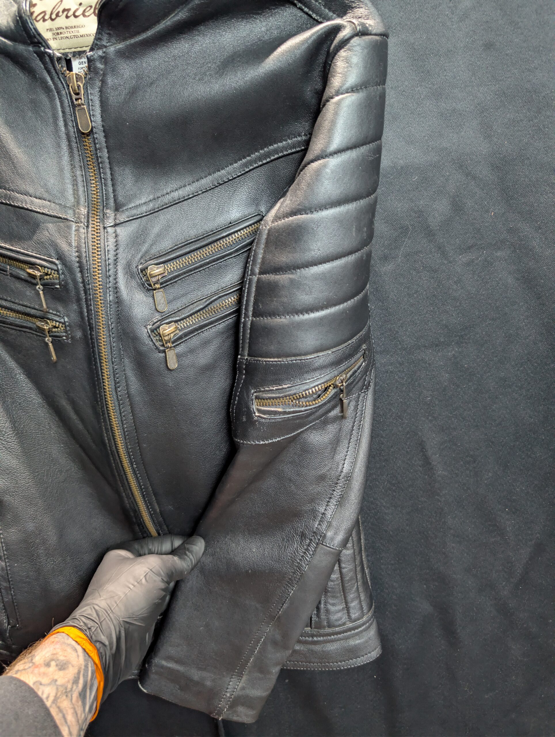 Black genuine sheepskin leather motorcycle jacket by Creaciones Gabriel featuring ribbed shoulder details and brass zipper pockets.