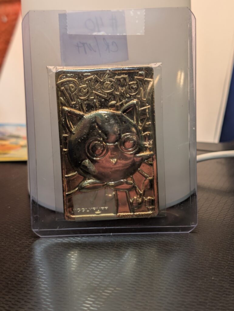 Vintage 1999 Burger King 23K gold-plated Jigglypuff Pokémon promotional trading card displayed in a clear protective case on a stand.