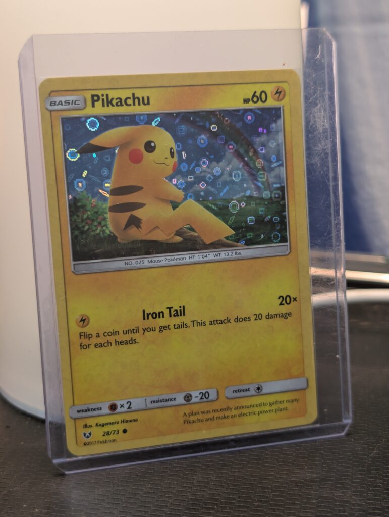 Holographic Pikachu Pokémon trading card, number 28/73 from the 2017 Shining Legends expansion, featuring the General Mills sequin holofoil pattern, displayed in a clear protective plastic sleeve.