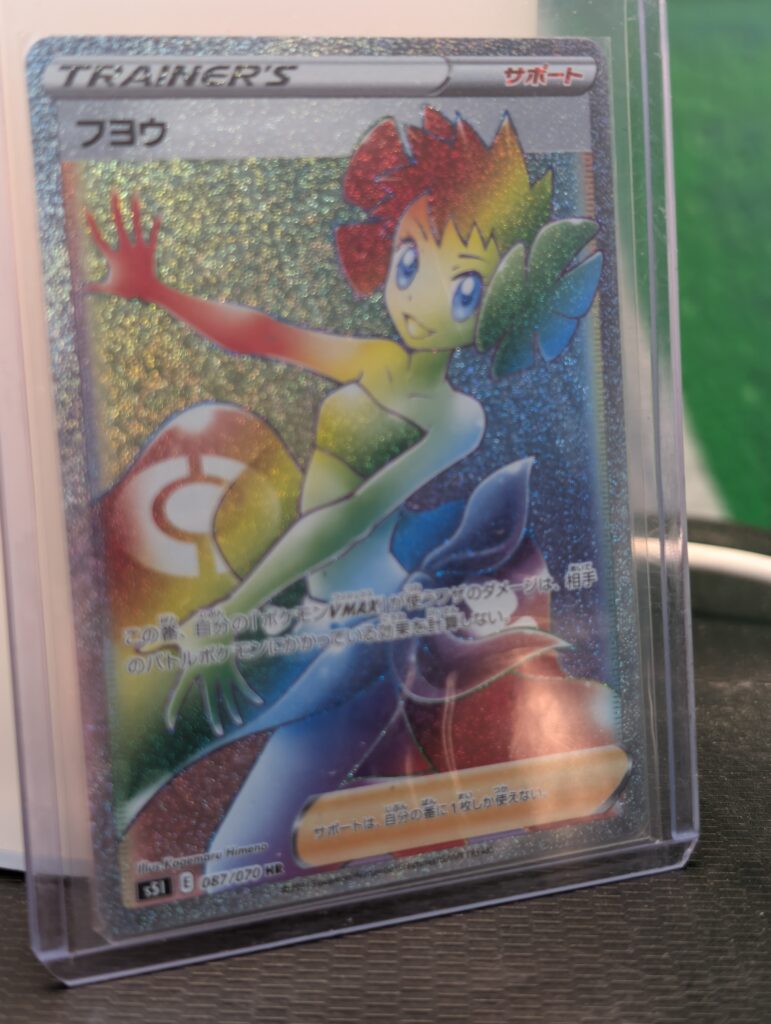 Stunning Japanese Phoebe Hyper Rare holographic trading card showing vibrant rainbow foil artwork of character inside clear protective display plastic sleeve against soft lighting for premium online listing