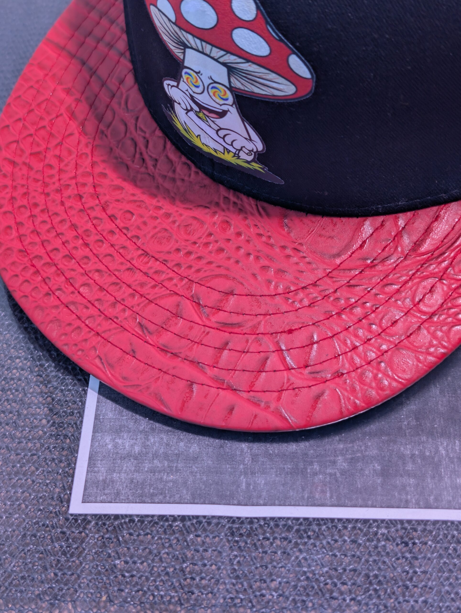 Black structured streetwear snapback hat featuring embroidered cartoon mushroom graphic alongside bright green dripping slime logo and textured red crocodile faux leather flat bill edge for style.