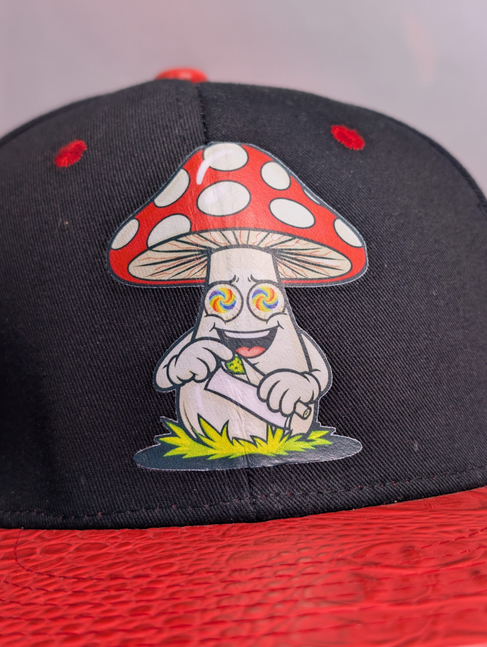 Black structured streetwear snapback hat featuring embroidered cartoon mushroom graphic alongside bright green dripping slime logo and textured red crocodile faux leather flat bill edge for style.