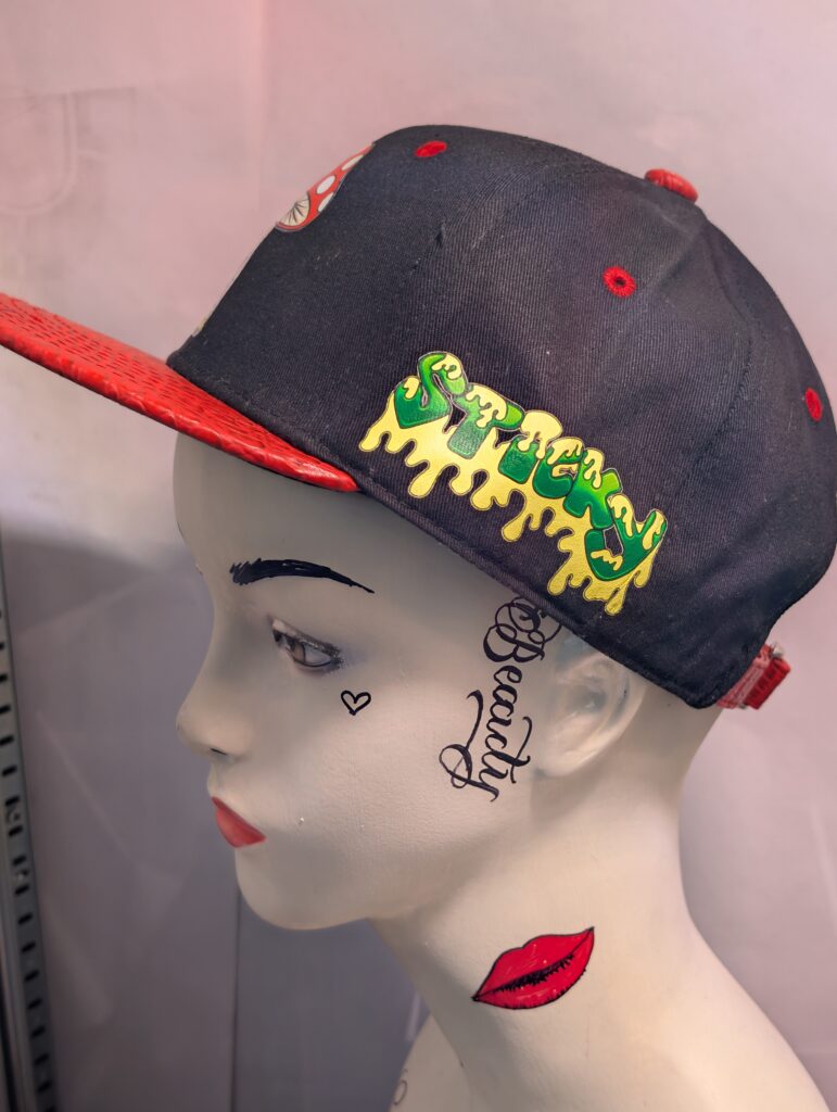 Black structured streetwear snapback hat featuring embroidered cartoon mushroom graphic alongside bright green dripping slime logo and textured red crocodile faux leather flat bill edge for style.