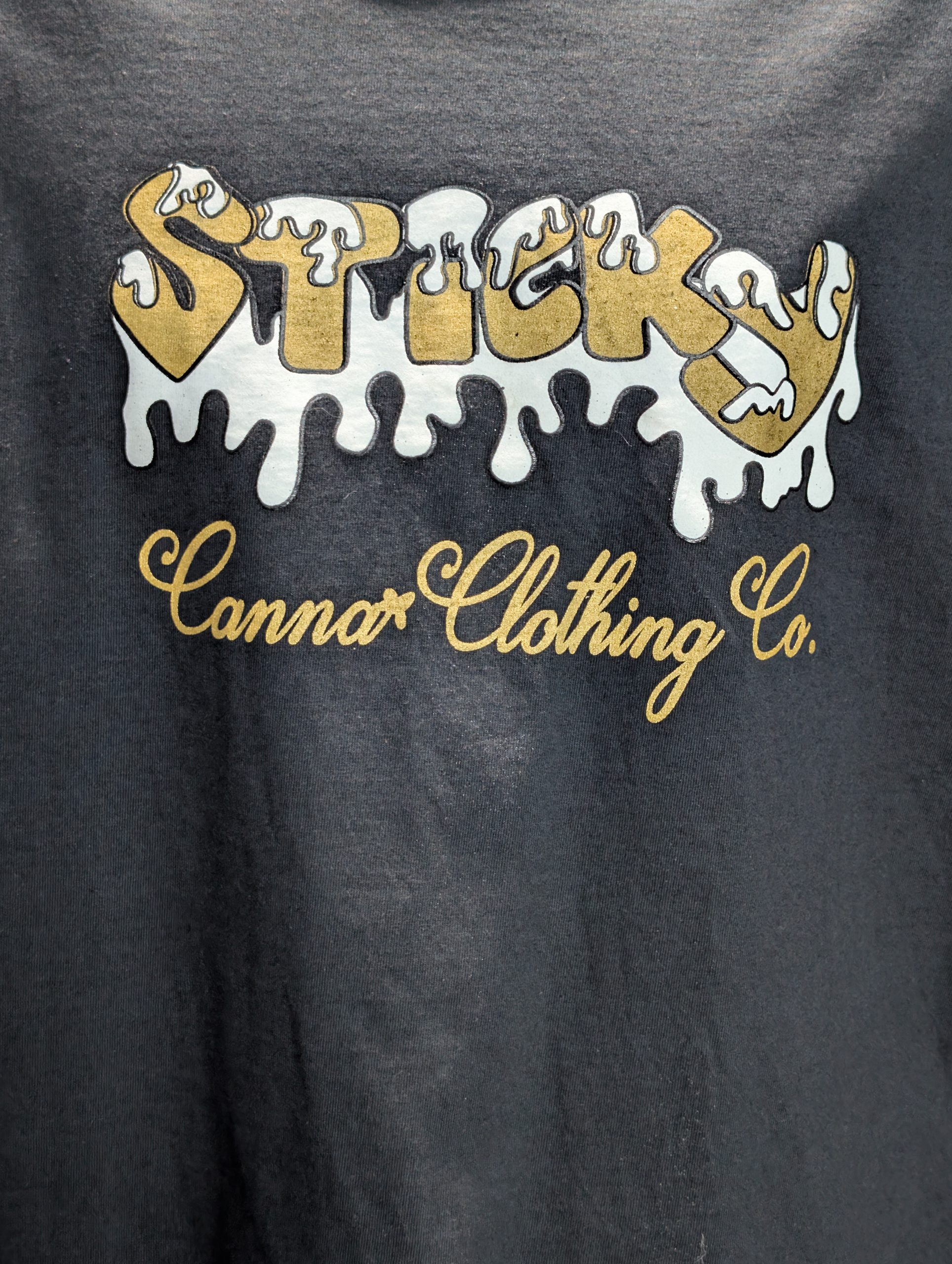 Black shirt featuring gold Sticky Canna drip logo.