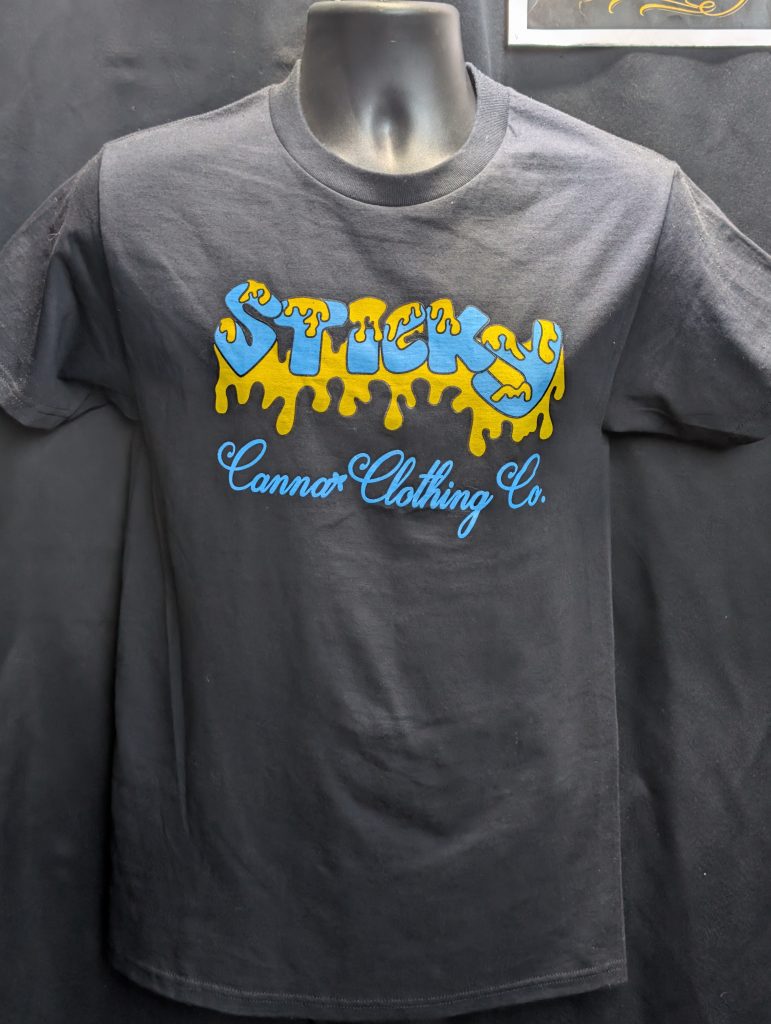 Black shirt featuring blue yellow Sticky Canna logo.