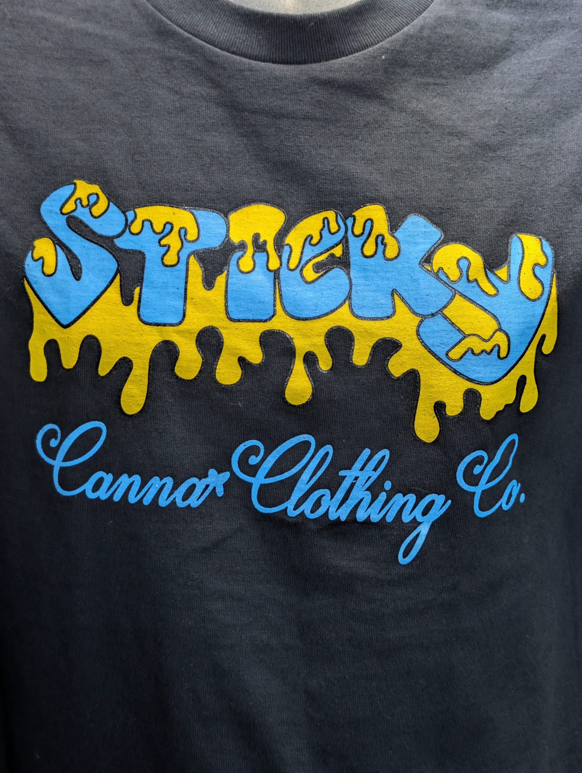 Black shirt featuring blue yellow Sticky Canna logo.