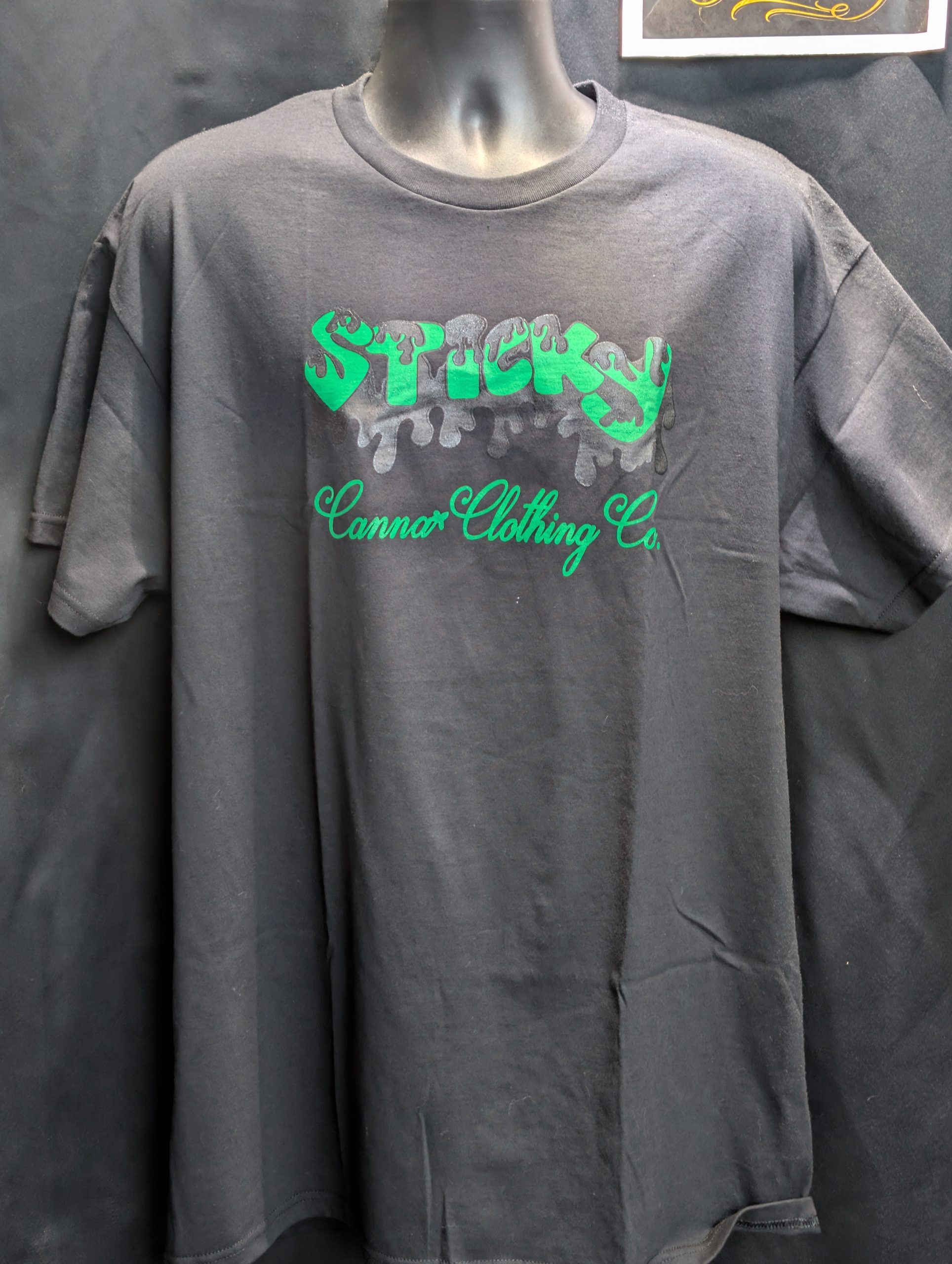 Black shirt featuring green Sticky Canna drip logo.
