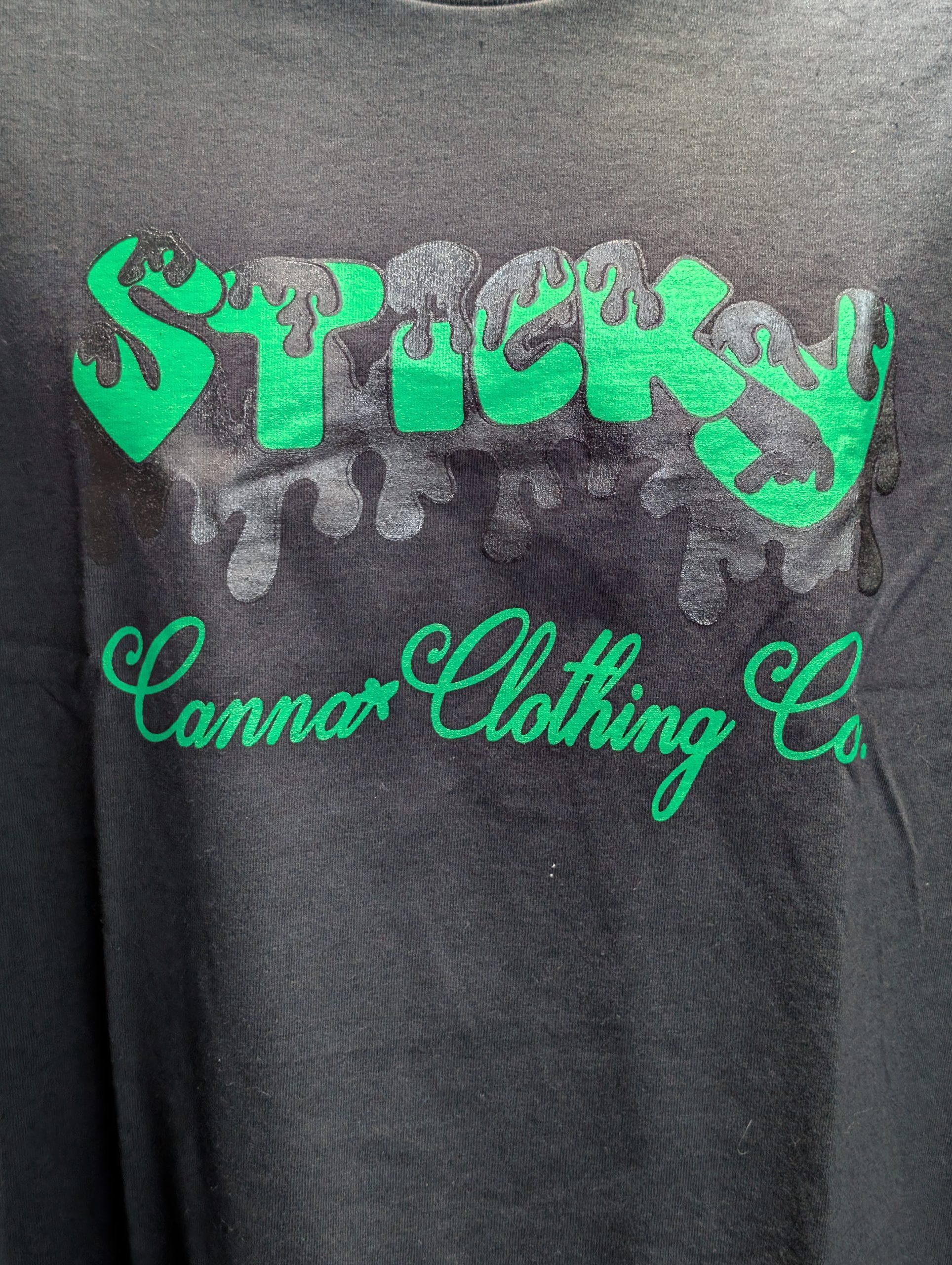 Black shirt featuring green Sticky Canna drip logo.