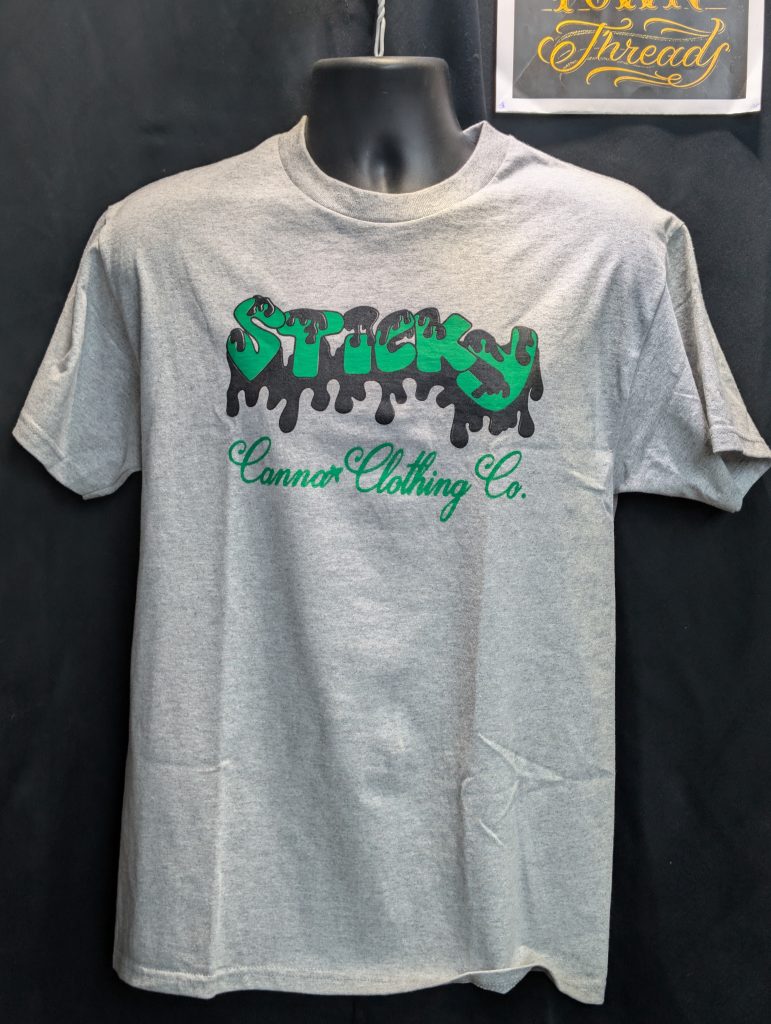 Grey shirt featuring green black Sticky Canna logo.