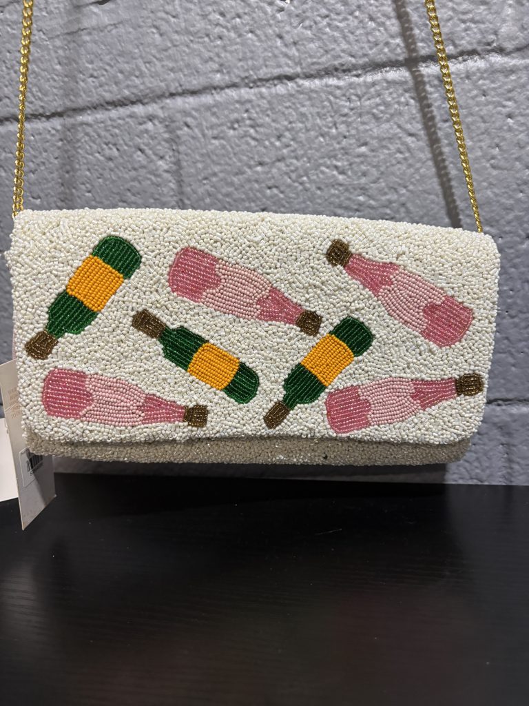 White beaded clutch featuring champagne bottle designs and a "POUR MORE" message on the interior.