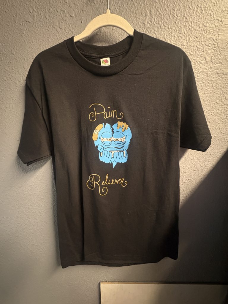 Black graphic t-shirt with "Pain Reliever" character design on front and blue swirl art on back, size M.