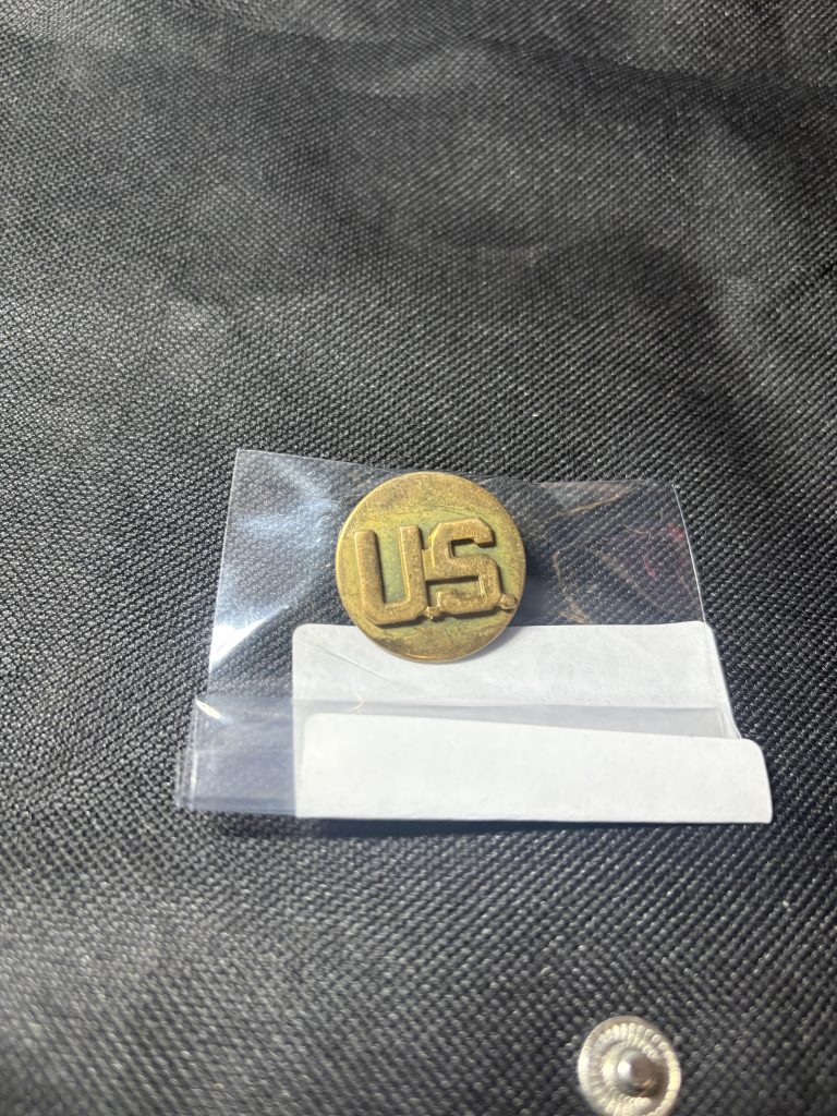 Vintage brass U.S. Army "U.S." collar insignia disc in a protective sleeve.