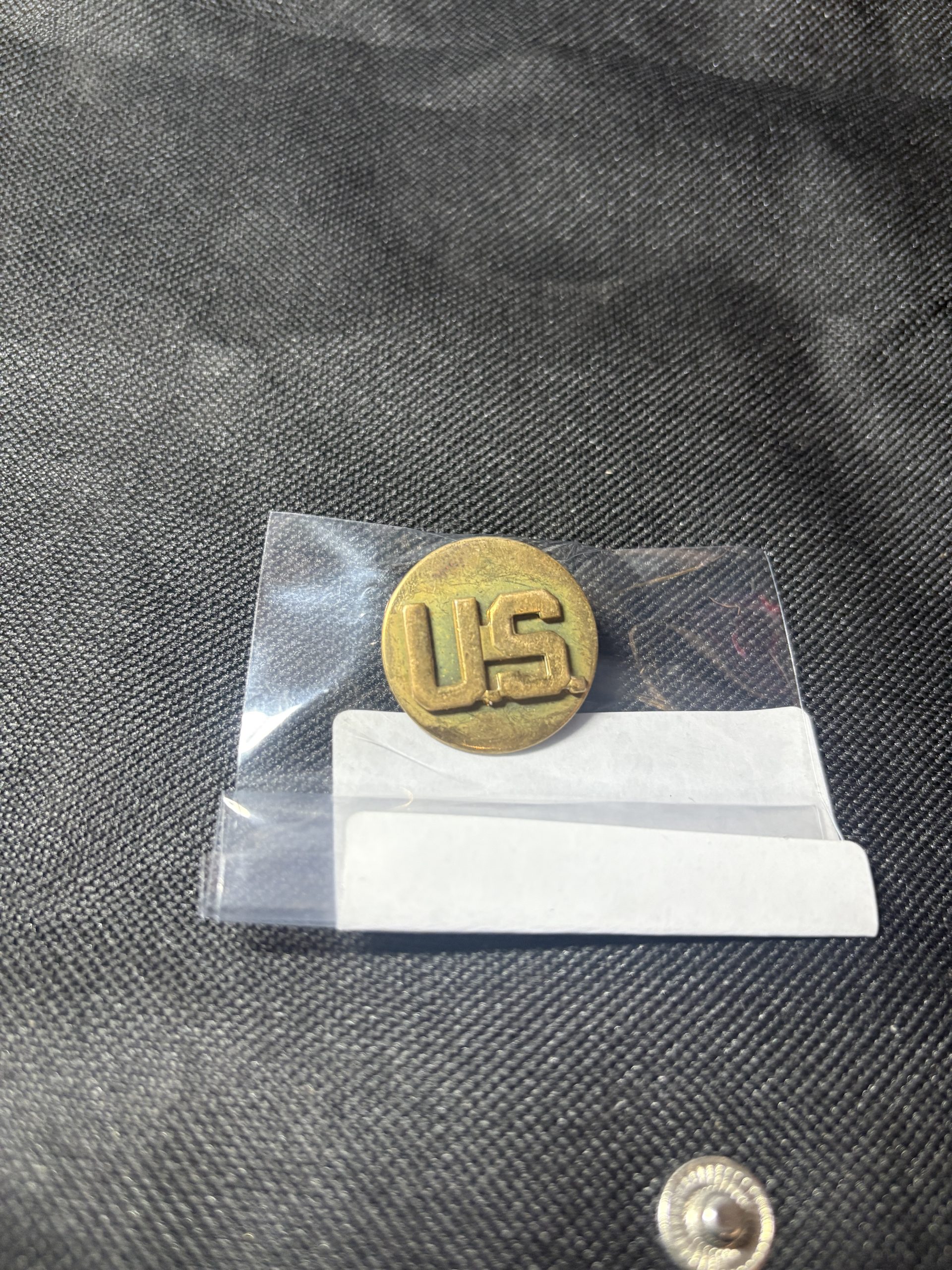 Vintage brass U.S. Army "U.S." collar insignia disc in a protective sleeve.