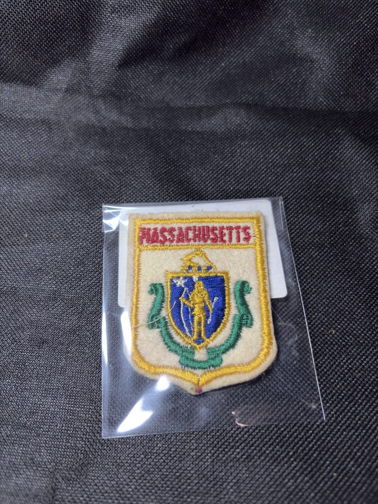 Vintage embroidered Massachusetts state seal patch with traditional heraldry design in a protective sleeve.