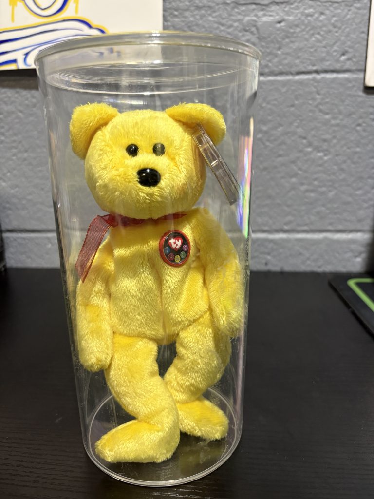 Ty Beanie Baby Tradee yellow bear with chest emblem in a clear display cylinder.