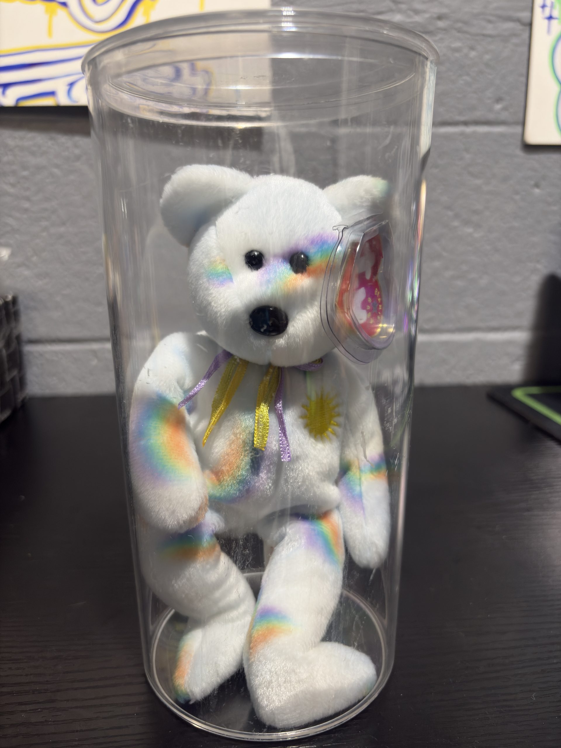 Ty Beanie Baby Cheery rainbow stripe bear with sun chest emblem in a clear display cylinder.