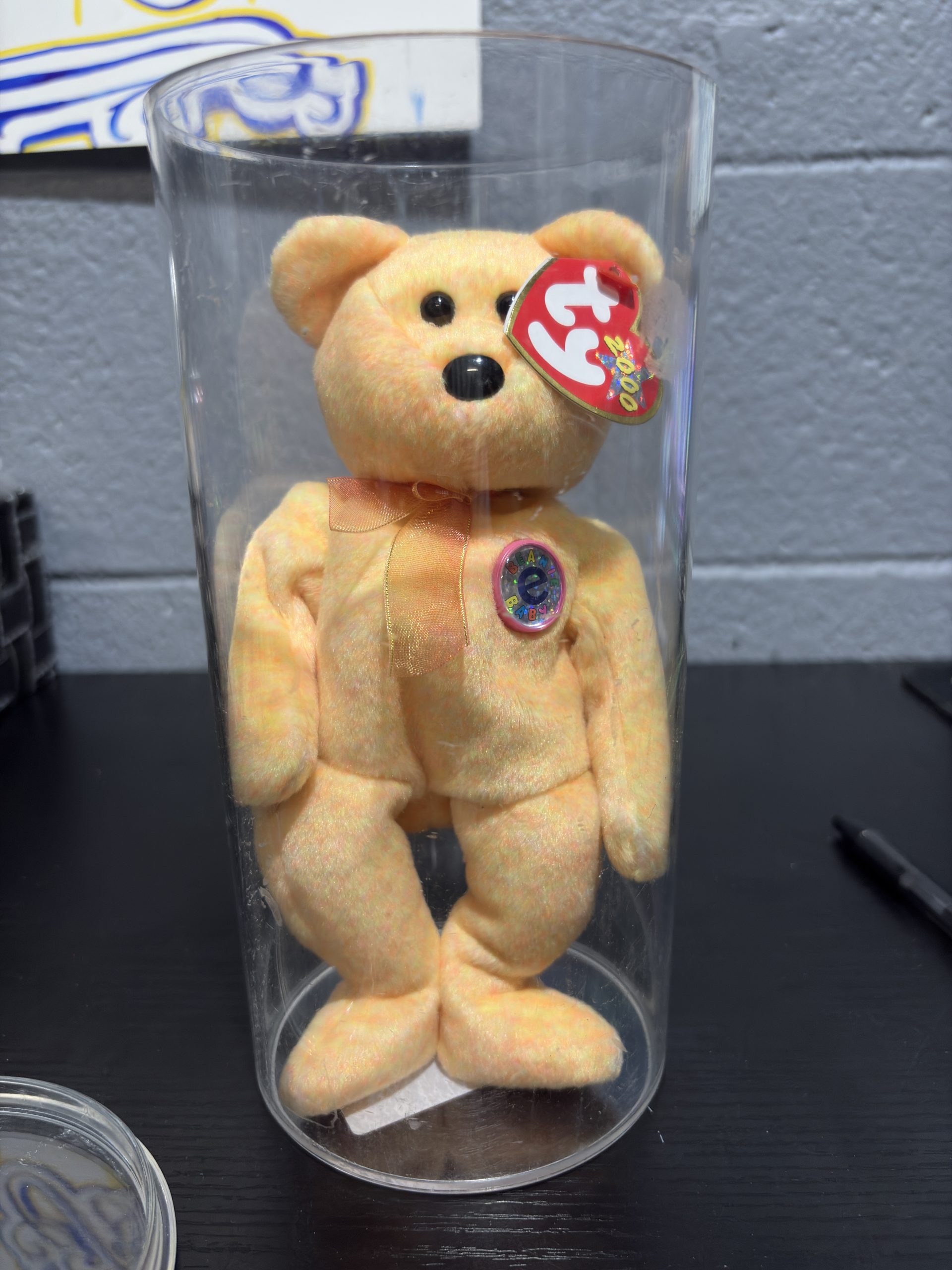Ty Beanie Baby Sunny yellow tie-dye bear with chest emblem in a clear display cylinder.