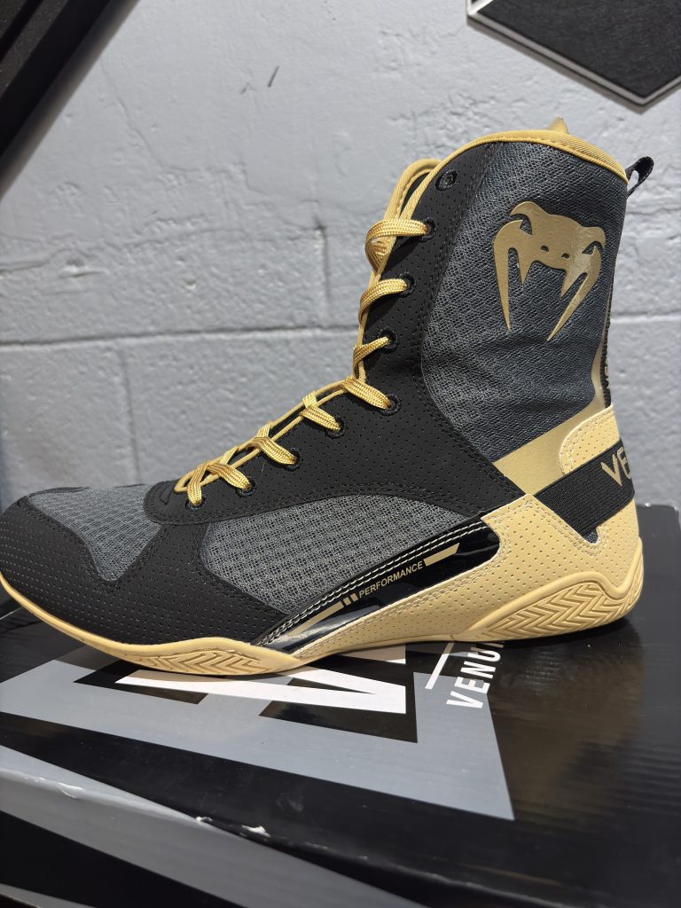 Venum Elite Boxing Shoes in Black and Beige on top of its branded shoebox.