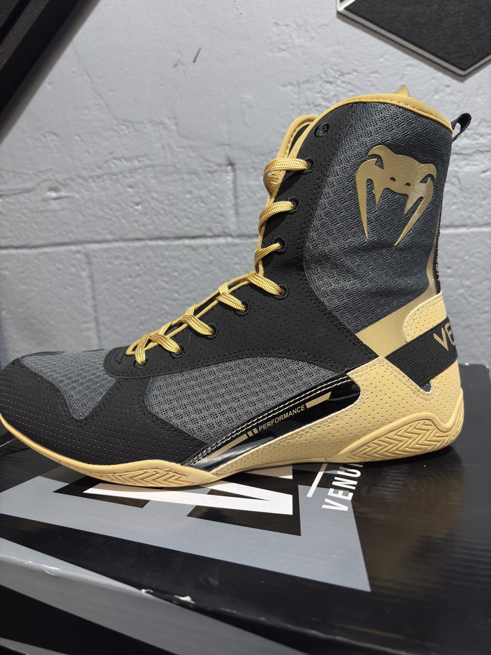 Venum Elite Boxing Shoes in Black and Beige on top of its branded shoebox.
