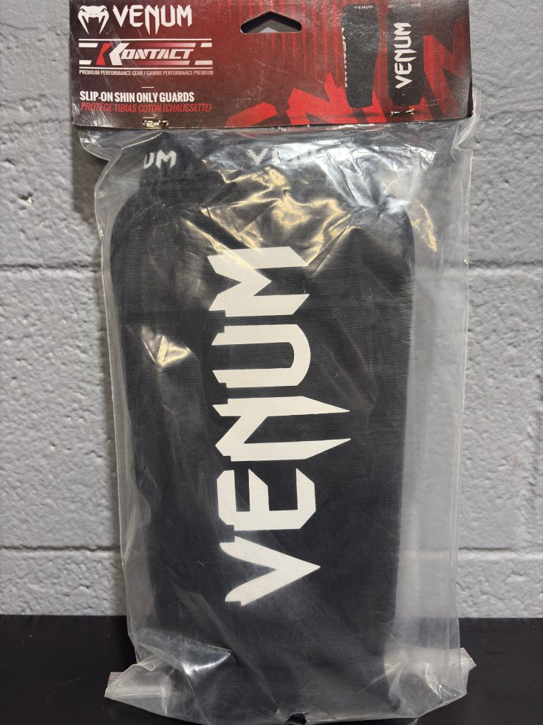 Venum Kontact Slip-On Shin Guards in black and white shown in and out of packaging.