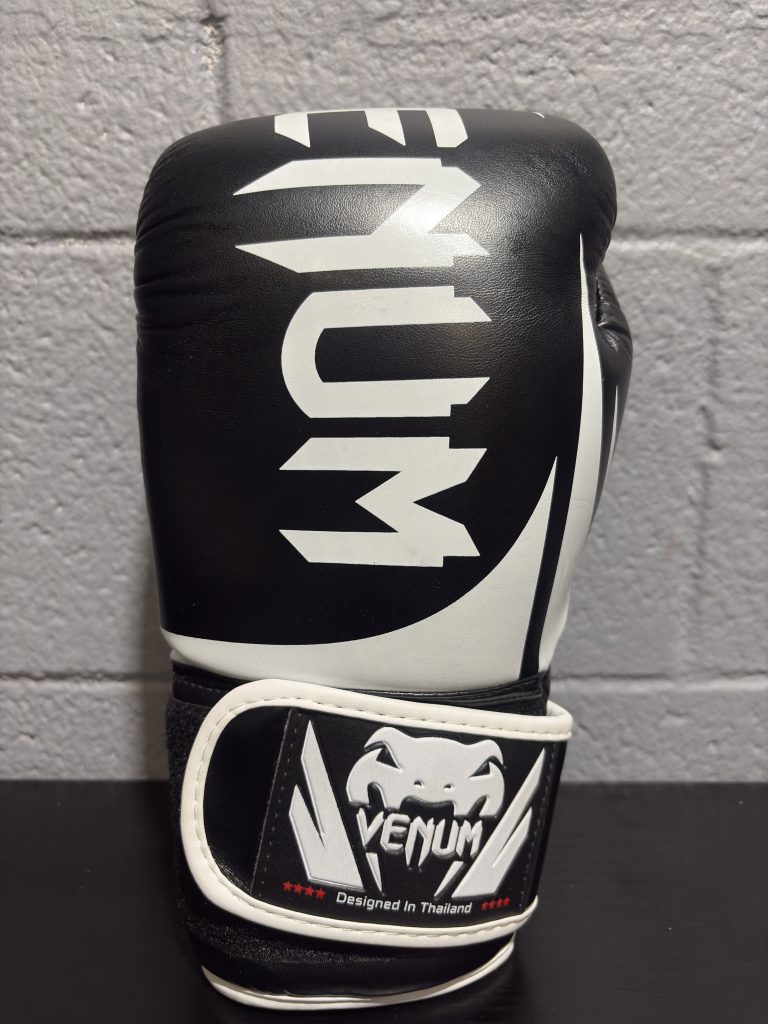 : Venum boxing gloves in black and white showing the striking surface and "Designed in Thailand" wrist badge.