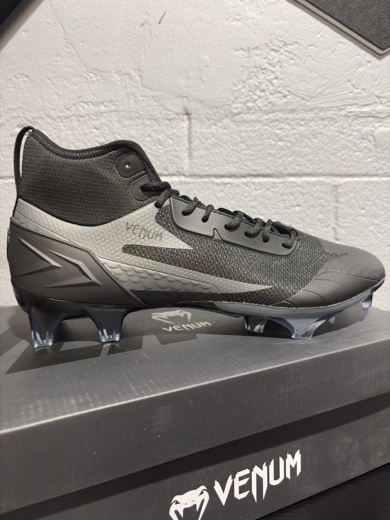Venum Elite Football Cleats in Black/Black displayed next to their branded shoebox.