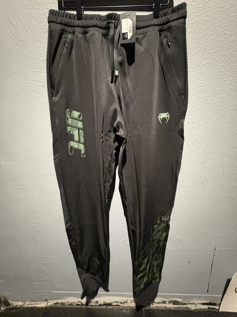 UFC Venum Authentic Fight Week Men's Pants in khaki and black showing the waistband tag, drawstrings, and leg logos in size XL.