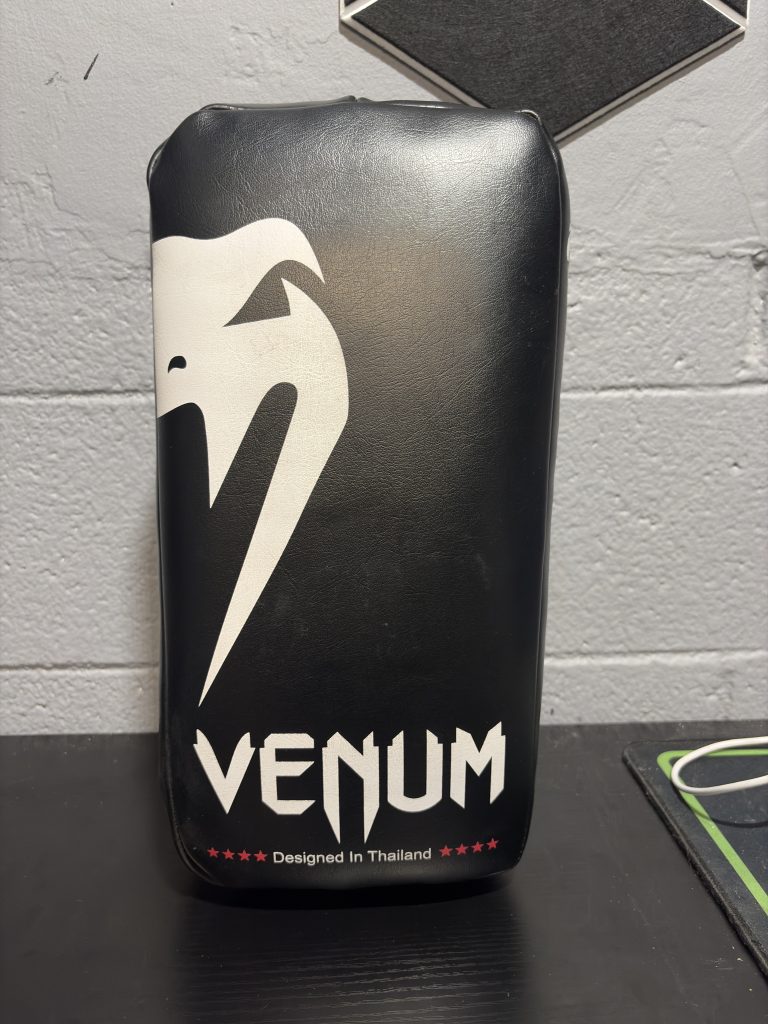 Venum Curved Kick Shield in Black and White showing the front snake logo and back handling straps.