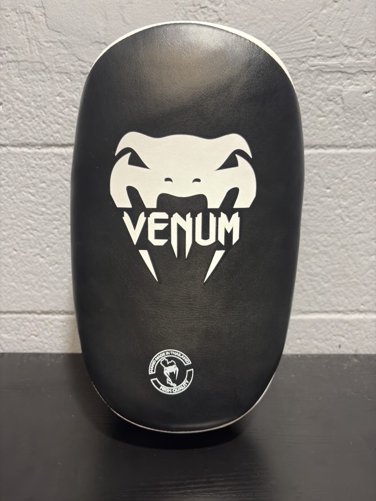 Venum Curved Kick Shield in Black and White showing the front logo stamp and back arm straps.