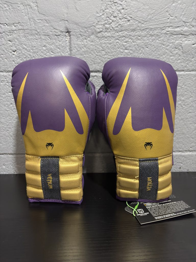Venum Reverso Boxing Gloves in Dark Purple and Gold showing the fist design, cuff details, and hanging retail tag in size 12oz.