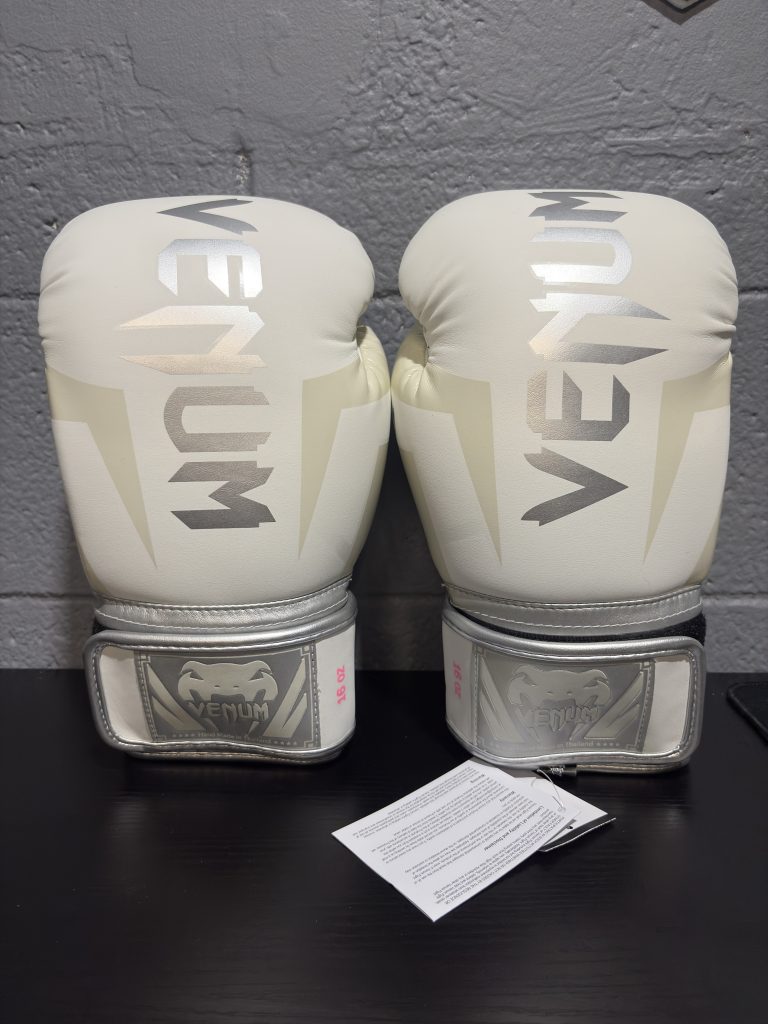 Venum Elite Boxing Gloves in White and Silver showing the fist design, cuff, and hanging retail tag in size 16oz.