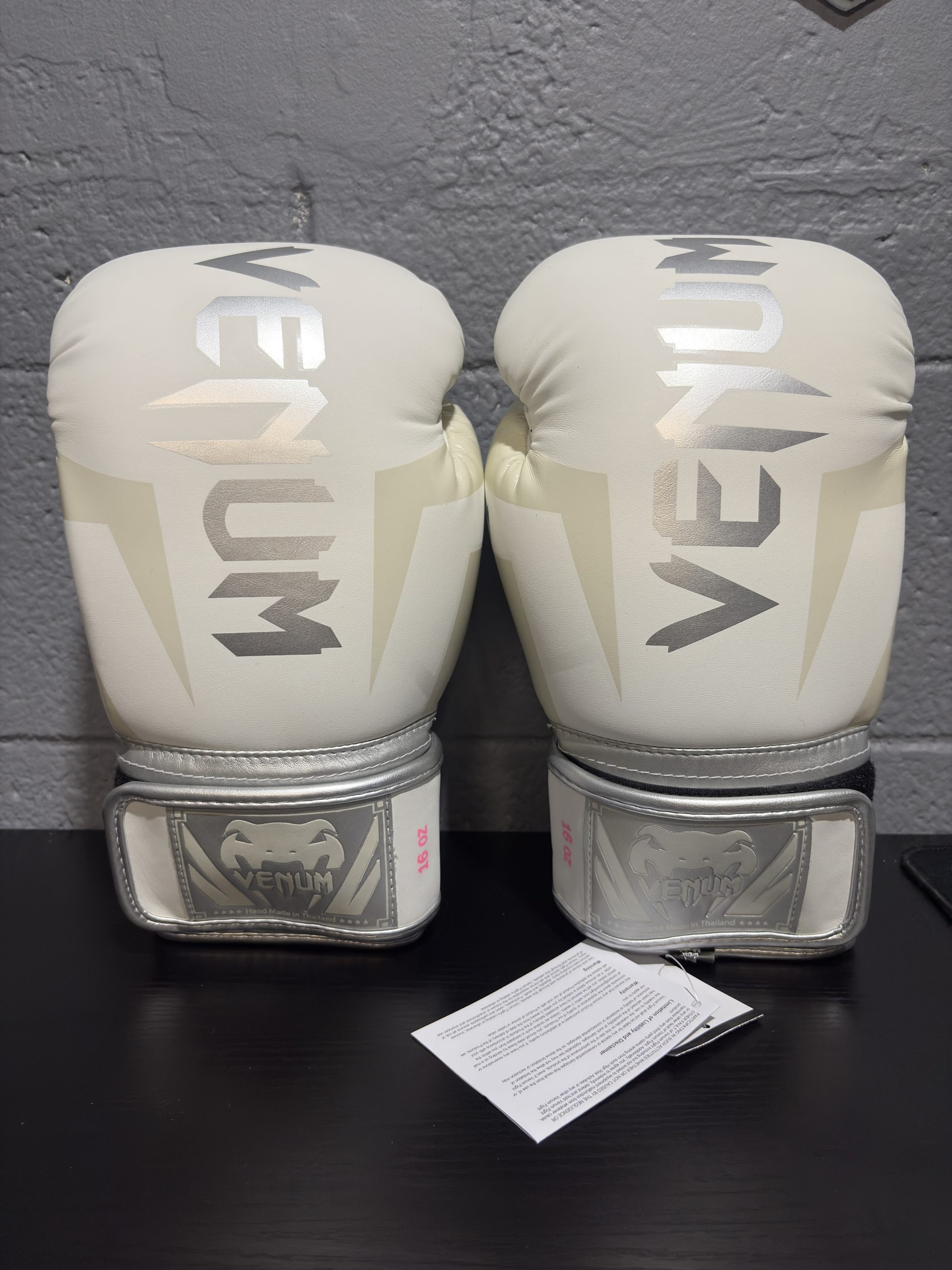Venum Elite Boxing Gloves in White and Silver showing the fist design, cuff, and hanging retail tag in size 16oz.