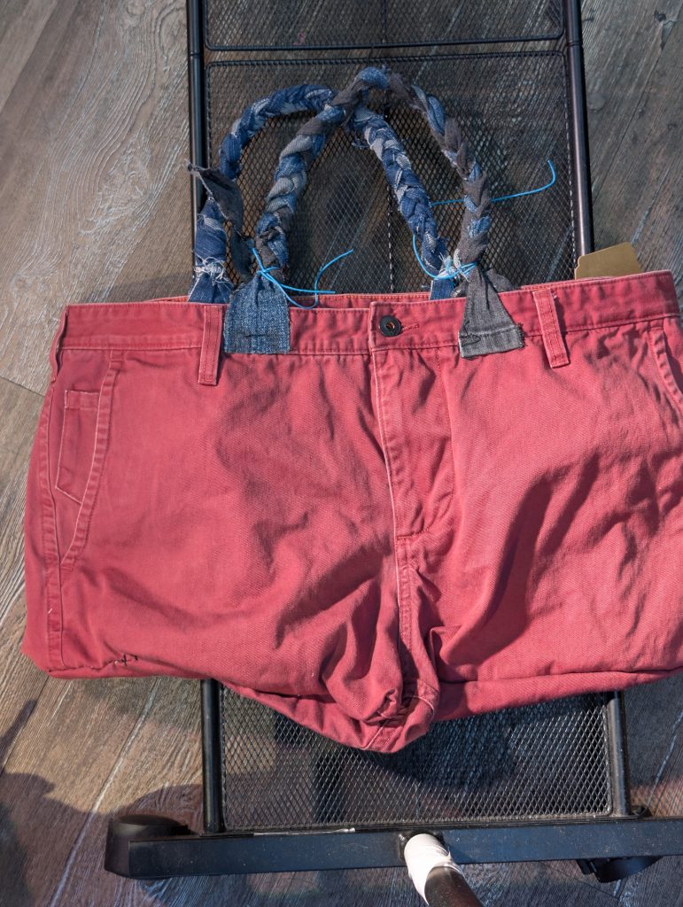 Upcycled Dockers pants tote bag in red maroon showing the front waistband, braided denim handles, and back patch details.