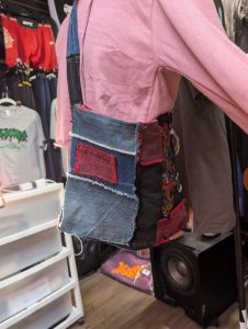 Upcycled patchwork denim crossbody bag showing the embroidered floral panel, mixed denim patches, and shoulder strap.