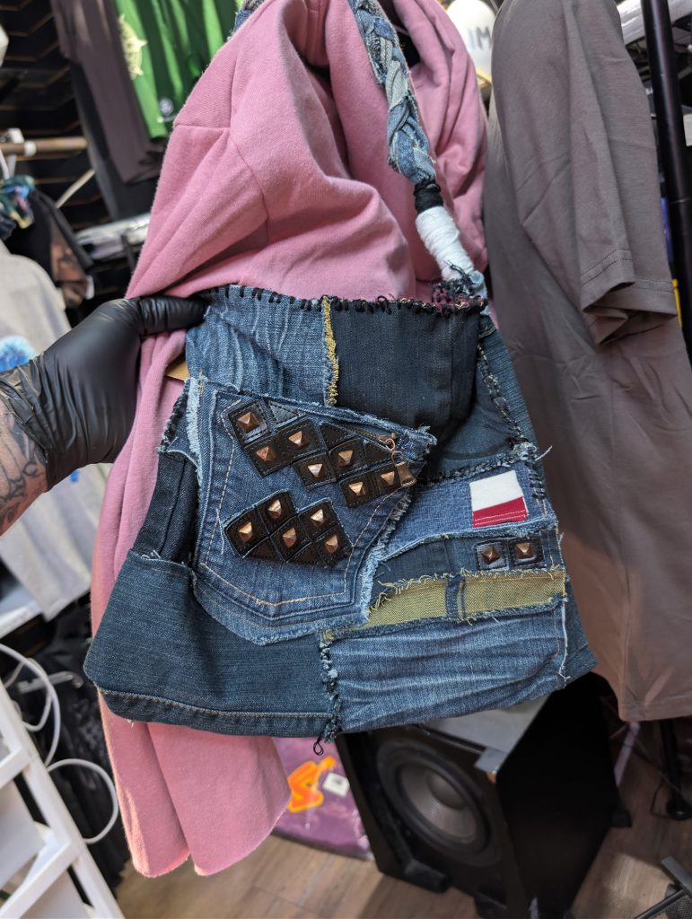 Upcycled patchwork denim shoulder bag showing the studded front pocket, mixed denim patches, and braided handles.