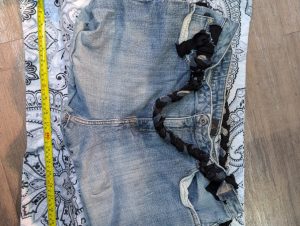 Upcycled distressed denim tote bag in blue showing the braided straps, patch details, and measurement tape.