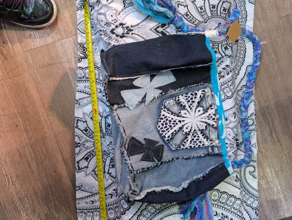 Upcycled patchwork denim crossbody bag showing the cross appliques, front pocket, and colorful braided strap.