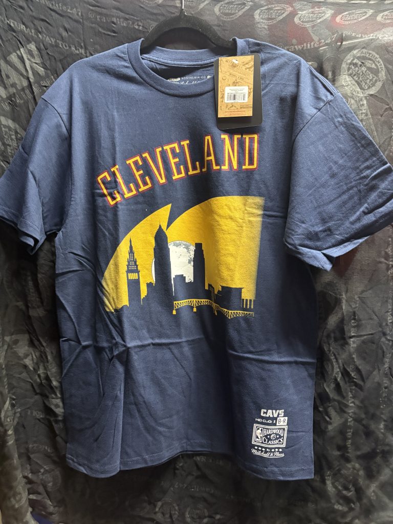 Kid Cudi x Bleacher Report x Mitchell & Ness Cleveland Cavaliers graphic t-shirt in navy blue showing the front skyline design and tag.